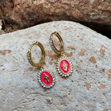 Load image into Gallery viewer, Huggie earrings with pink central stone and gold Virgin Mary surrounded by cubic zirconia laying on a stone.
