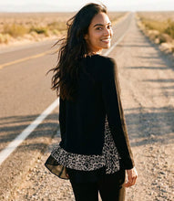Load image into Gallery viewer, A woman stands on a desert road wearing a black long-sleeve top with a leopard-print ruffle hem, photographed from behind as she looks back over her shoulder.
