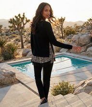 Load image into Gallery viewer, A woman stands on outdoor stone steps beside a swimming pool in a desert landscape, wearing a black long-sleeve sweater with a leopard-print hem, black pants, and black shoes.
