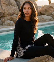 Load image into Gallery viewer, A woman sits on the edge of a swimming pool wearing a black long-sleeve top with a leopard-print side panel and black leggings, set against a background of large rocks and the blue pool water.
