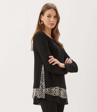 Load image into Gallery viewer, A woman modeling a black long-sleeve top with a leopard-print ruffle trim at the hem, posed against a plain white studio background.
