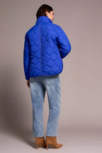 Load image into Gallery viewer, Woman wearing a blue puffer jacket, blue jeans and tan suede boots against a neutral background.
