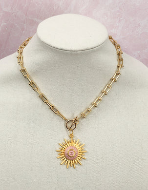 Introducing the dazzling Lilian necklace! This extraordinary piece features a vintage round Chanel button in soft pink and gold, beautifully nestled on a radiant gold sunburst base. This vibrant and cheerful necklace is truly unique and will add a touch of elegance to any ensemble. 