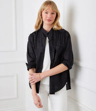 Load image into Gallery viewer, Woman wearing a black blouse over a white top and white pants against a white paneled wall.

