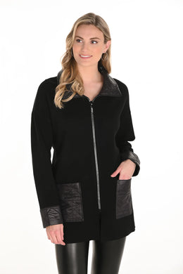 Woman wearing a long black jacket with rhinestone zipper and black leather leggings against a white background.