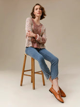Load image into Gallery viewer, A woman sits on a wooden stool wearing a textured, multicolor knit sweater, blue cropped jeans, and brown leather loafers against a neutral beige studio background.
