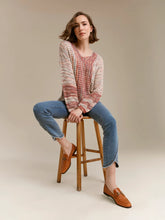 Load image into Gallery viewer, A woman sits on a wooden stool wearing a chunky knit sweater in multicolor paired with blue jeans and tan loafers, against a solid beige studio background.
