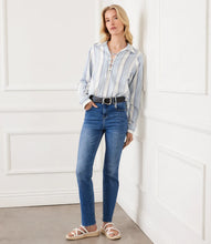 Load image into Gallery viewer, Woman wearing a blue and white striped shirt with a lace-up front, blue jeans, black belt and cream-colored sandals standing against a white wall.
