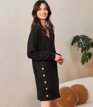 Load image into Gallery viewer, Woman wearing a black dress with gold buttons against a neutral background.
