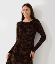 Load image into Gallery viewer, A woman wearing a long-sleeve dark brown velvet dress, leaning against a light gray wall.
