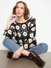 Load image into Gallery viewer, A woman sits cross-legged on a gray floor against a white wall, wearing a black crochet top with a white daisy pattern, blue jeans, and dark brown ankle boots.
