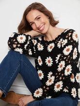 Load image into Gallery viewer, A woman wearing a black crochet knit sweater with a white daisy pattern, paired with blue jeans and brown suede boots, sitting against a white wall.
