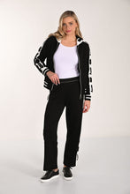 Load image into Gallery viewer, Woman wearing a black and white tracksuit and black tennis shoes with a white background.
