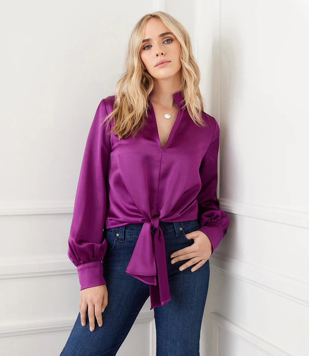 This top is crafted from a silky fabric and features a stand-up collar and tie waistband for an elegant aesthetic. The remarkable Magenta color adds a bold statement to any look, whether you choose to dress it up or down with denim.  Color - Magenta. Blouson Sleeve. Tie at waist. Button down. No pockets. Long sleeve. Satin fabrication.