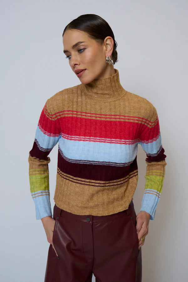 Woman wearing a colorful striped sweater and burgundy faux leather pants against a plain background.