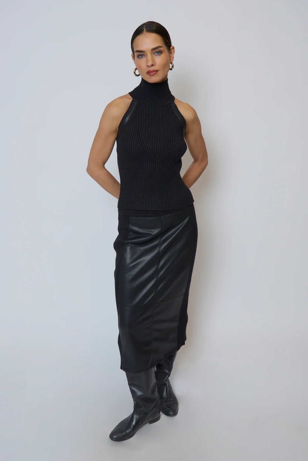 Woman wearing a black sleeveless top, leather skirt and black boots against a white background.