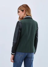 Load image into Gallery viewer, Woman wearing a green jacket with black sleeves and blue jeans against a light gray background.
