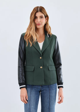 Woman wearing a green blazer with black leather sleeves against a light gray background.