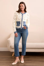 Load image into Gallery viewer, Woman wearing an eggshell cardigan with blue denim accents, blue jeans and beige heels standing in a room. 
