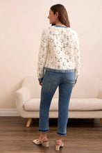Load image into Gallery viewer, Woman wearing an eggshell cardigan with blue denim accents, blue jeans and beige heels standing in a room with a beige chair in the background.
