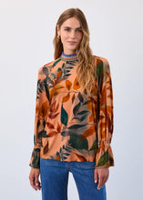 Load image into Gallery viewer, Woman wearing a leaf patterned blouse and blue jeans against a neutral background.
