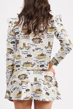 Load image into Gallery viewer, A woman from the back modeling a matching long-sleeve collared top and skort set with a white base and a gold, black graphic print, set against a plain light gray background.
