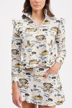 Load image into Gallery viewer, A woman modeling a matching long-sleeve collared top and skort set with a white base and gold and black graphic print, set against a plain light gray background.
