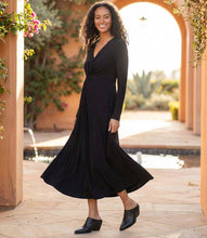 Load image into Gallery viewer, Woman in a black twist front, midi dress and black shoes standing outdoors with a pool and garden in the background.
