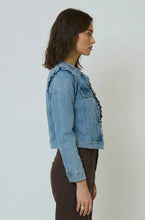 Load image into Gallery viewer, Woman wearing a denim jacket with ruffle trim and brown pants against a plain background.
