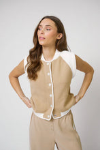 Load image into Gallery viewer, Woman wearing a sand-colored sleeveless sweater vest with beige pants on a plain background.
