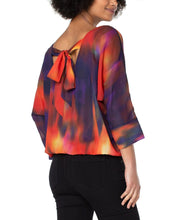 Load image into Gallery viewer, Featuring mesmerizing northern lights print in red, purple/blue, yellow and black, this top is sure to turn heads. Its dolman sleeves and tie back detail add to its charm — perfect for brunch or special occasions, it looks great when paired with denim or trousers.  `Colors-Northern lights - Splashes of red, purple/blue, yellow and black. Chiffon fabrication Round neckline. 3/4 dolman sleeves. Northern light print. Tie back detail. Gathered hemline.
