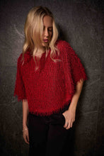 Load image into Gallery viewer, Woman wearing a red fringe sweater and black pants against a dark background.
