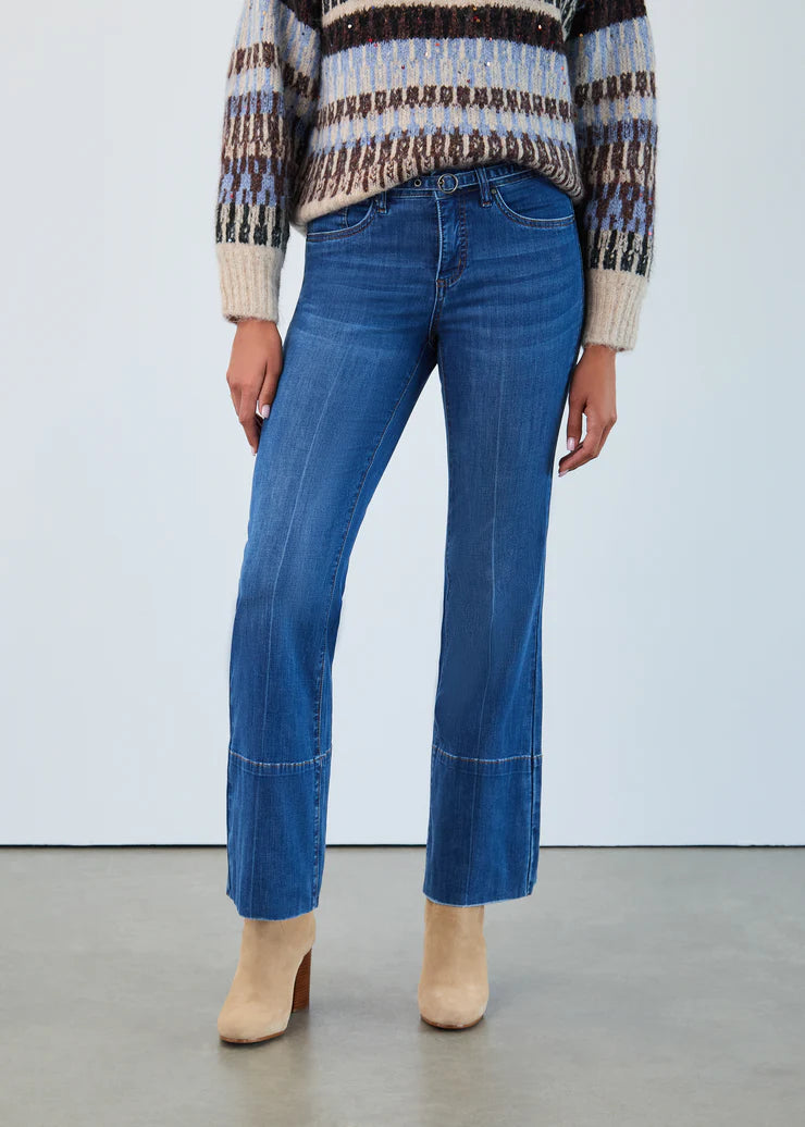 Model wearing blue jeans, a patterned sweater and tan suede boots against a white background.