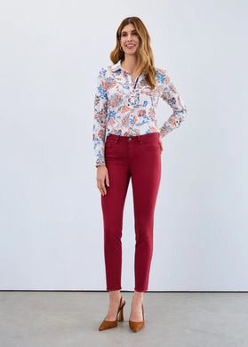 Woman wearing a floral blouse, red slim ankle jeans and brown heels against a white background.