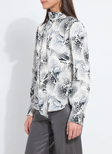 Load image into Gallery viewer, Model wearing a patterned blouse with tie scarf and grey pants against a white background.
