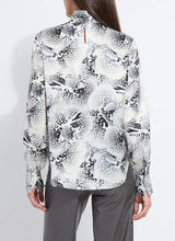 Load image into Gallery viewer, Model wearing a patterned blouse with tie scarf and grey pants against a white background.
