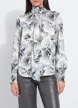 Load image into Gallery viewer, Model wearing a patterned blouse with tie scarf and grey pants against a white background.
