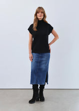Load image into Gallery viewer, Woman wearing a black cap sleeve, mock neck top, blue jean skirt and black boots against a light gray background.
