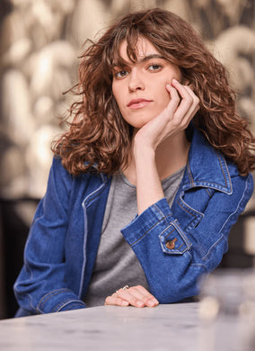 Woman wearing a denim trench coat and grey tee with a blurred background.