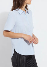 Load image into Gallery viewer, A woman wearing a light blue short-sleeve button-up shirt and black-and-white pinstriped trousers, shown from the side against a plain white background.
