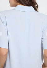 Load image into Gallery viewer, Close-up back view of a person wearing a light blue short-sleeve collared top against a plain light background.
