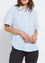 Load image into Gallery viewer, A woman wearing a light blue short-sleeve button-up shirt and black-and-white pinstriped trousers, shown from the mouth down against a plain white background.
