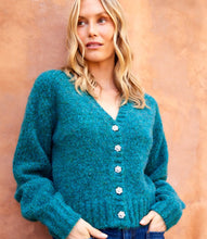 Load image into Gallery viewer, Woman wearing a teal cardigan with pearl buttons and jeans against a beige wall.
