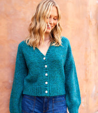 Load image into Gallery viewer, Woman wearing a teal cardigan with pearl buttons and jeans against a beige wall.
