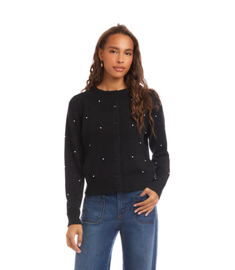 Woman wearing a black sweater with pearl embellishments and blue jeans against a white background.