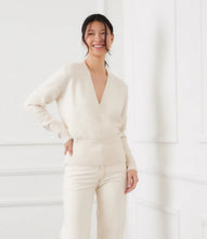 Load image into Gallery viewer, Woman wearing a cream v-neck  sweater with pearls and cream pants standing in front of a white wall.

