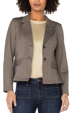 Woman wearing a brown pinstripe blazer over a beige top and blue jeans against a white background.