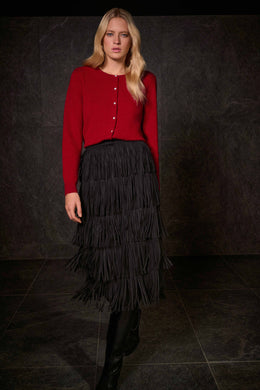 Woman wearing a red cardigan and black tiered fringe skirt and black boots against a dark background.