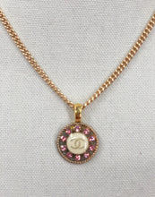 Load image into Gallery viewer, Discover the exquisite style of the Posey Pink and Gold Vintage Chanel Button Necklace from Modern Vintage Creations. Featuring a captivating design with sparkling pink crystals surrounding a white base adorned with the iconic gold CC logo, this necklace is a truly unique and desirable piece.

