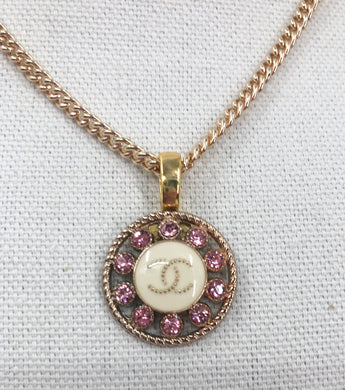 Discover the exquisite style of the Posey Pink and Gold Vintage Chanel Button Necklace from Modern Vintage Creations. Featuring a captivating design with sparkling pink crystals surrounding a white base adorned with the iconic gold CC logo, this necklace is a truly unique and desirable piece.